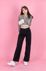 Portrait studio shot of Asian trendy fashionable female hipster teen model in casual crop top street wears jacket sunglasses carrying leather handbag purse standing look at camera on pink background