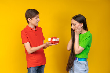 Smiling couple two friends guy and girl in casual clothes isolated on yellow background. Valentine's day female birthday holiday concept. Hold gift box with gift ribbon bow looking at each other