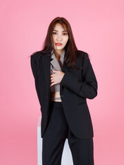 Portrait studio shot of Asian beautiful urban trendy modern fashionable long hair female hipster teenager model in casual black suit with crop top shirt standing look at camera on pink background