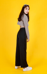 Fototapeta premium Portrait studio full body shot of Asian urban trendy modern fashionable long hair female hipster teen model in casual street wears crop top shirt standing posing look at camera on yellow background