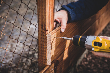 man drills a hole in a wooden board, project raising bed