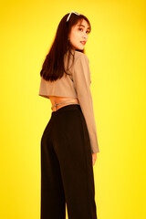 Naklejka premium Portrait studio shot of Asian trendy fashionable female hipster teen model in casual crop top street wears jacket sunglasses sneakers holding handbag purse look at camera on yellow background
