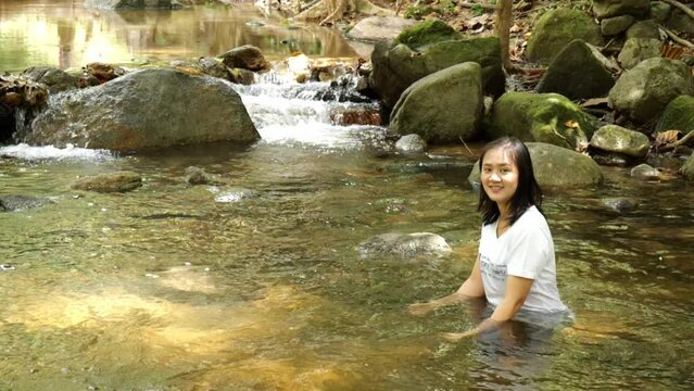 Take a slow motion photo of an Asian woman hanging out at a waterfall. She wants to have fun on vacation. The waterfall is very cold because it is natural water.