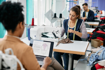 Young seamstress adjusts thread on sewing machine while working in clothing design workshop.