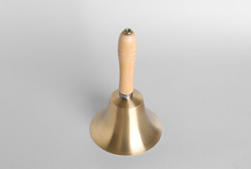 Golden school bell with wooden handle on grey background