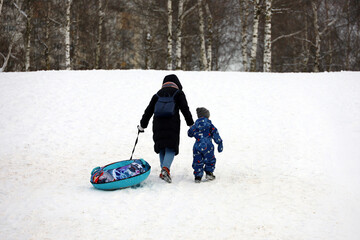 Woman with child climb the slide to roll down it on snow tube. Mother and son having fun in winter park