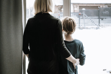 Mom and son standing near winter window at home. Cold season beauty.