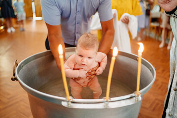 the baby boy is lowered into a font with holy water at baptism in the church. 
