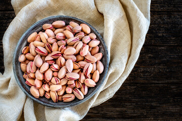Many pistachios on the old rustic wooden bowl. Dried nuts concept. 