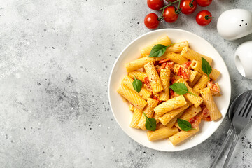 Tortiglioni with tomatoes, ricotta and basil in a white plate on a light kitchen table. Traditional Italian pasta with vegetables and creamy cottage cheese in a bowl. Top view	