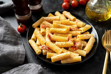 Tortiglioni with tomatoes, ricotta and basil in a black plate on a dark kitchen table. Traditional Italian pasta with vegetables and creamy cottage cheese on a culinary background