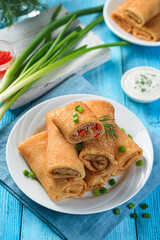 Thin fried pancakes with meat filling with onions and dill on a blue background. Side view, vertical.