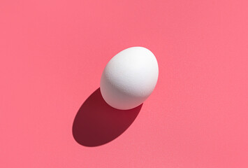 A white egg with a hard shadow on a pink background. The concept of Easter, minimalistic food.