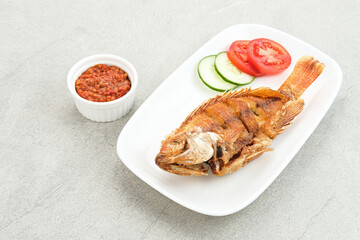 Fried Tilapia or Ikan Nila Goreng. Served on white plate with sambal (chilli sauce), cucumber and tomato slice. Selected focus.
