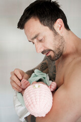 Young strong bare chested father with tattoo covering his shoulder and arm holds his newborn baby...