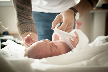 Close up of a father’s tattooed arms and hand wrapping up his newborn baby girl with a blanket on...