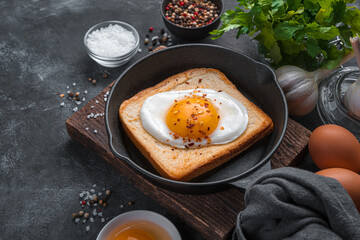 Fried egg on fried toast on a dark background with spices and fresh herbs. Side view, copy space.