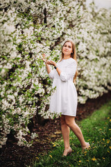 Beautiful young woman near blooming white tree in spring park. A woman in a white dress stands among the flowers on an apple tree. spring season concept