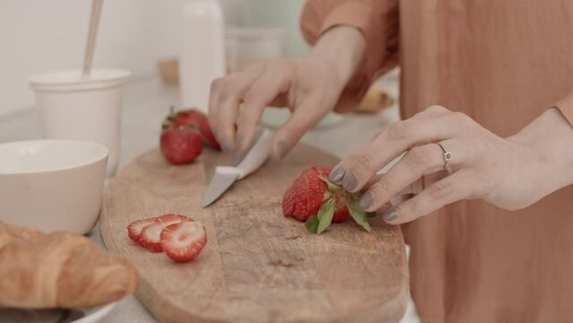 Slowmo closeup of unrecognizable woman cutting up some fresh strawberries while making breakfast at home
