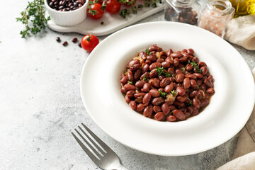 Stewed red beans with onion and thyme in tomato sauce in a white plate on the kitchen table closeup	