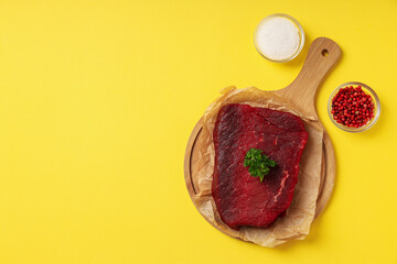 Concept of tasty food with with raw beef steak on yellow background