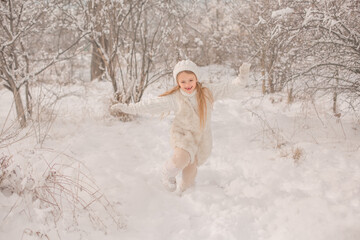 a happy little girl in a white knitted hat and sweater runs around a snowy park