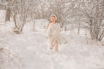 Fototapeta na wymiar a happy little girl in a white knitted hat and sweater runs around a snowy park