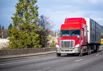Fototapeta na wymiar Bright red big rig semi truck transporting cargo in semi trailer running on the turning highway road