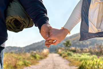 Close up of loving couple holding hands while walking on rural road in autumn or spring nature. Friendship and relationship concept. Well Being and unity with nature. Road to mountain.