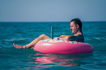 Remote work on vacation at sea. Businessman working with laptop on inflatable ring in the water of ocean.