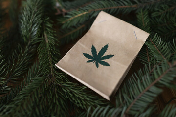 Paper bag with marijuana lying among green christmas tree branches closeup