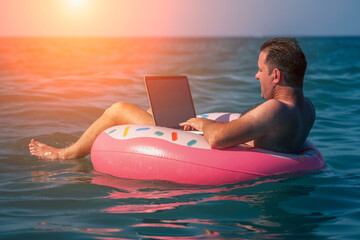 Man with a laptop on inflatable ring in the water of sea or ocean