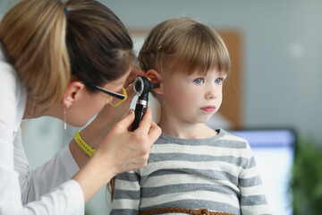 Female pediatrician looking at ear of little girl using otoscope in clinic - obrazy, fototapety, plakaty