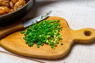 chopped green onions and fried potatoes in a frying pan, cooked food in a rustic style on a background of white wooden boards