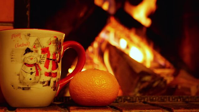 cup with Christmas ornament and tangerine. the fireplace is blurred in the background. 4k video