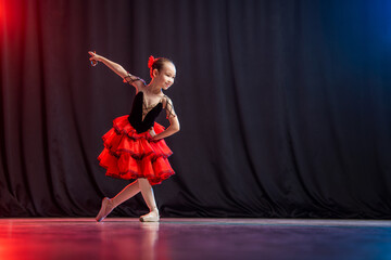 A little girl ballerina is dancing on stage in a tutu on pointe shoes with castanedas, the classic...