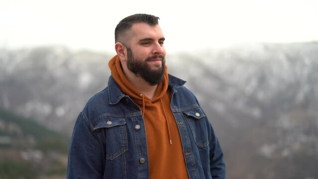 Chico alto con barba posando y sonriendo con paisaje nevado de fondo