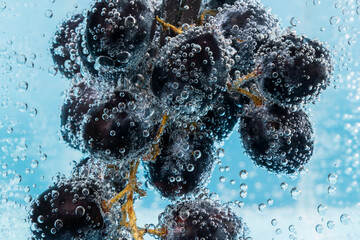 Black grapes in water with air bubbles close up macro. Juicy summer fruit cocktail