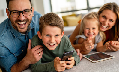 Happy young family having fun time at home. Parents with children using digital device.