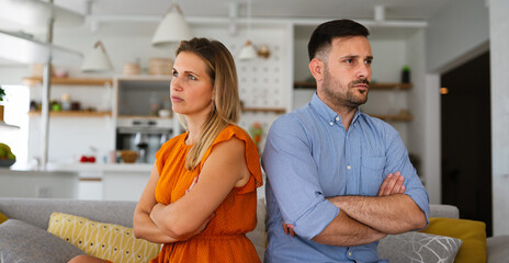 Sad pensive couple thinking of relationships problems sitting on sofa, conflicts in marriage.