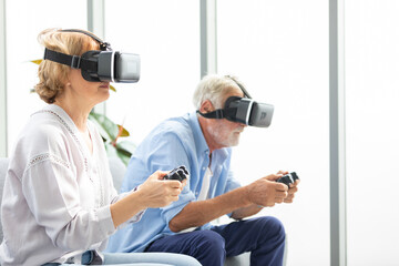 senior couple wearing virtual reality goggles headset (VR) and holding game controller for play a game