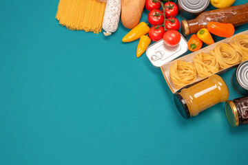 Food bank, food delivery concept. Different groceries, food donations on green background with copy space - pasta, fresh vegatables, canned food, baguette and other groceries