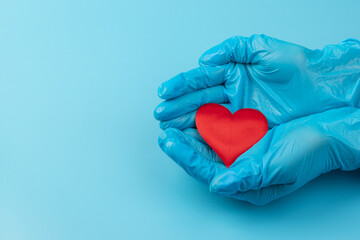 Red heart in hands in blue medical gloves on blue background. Background for the day of the medic. World Heart Day. Heart diseases.