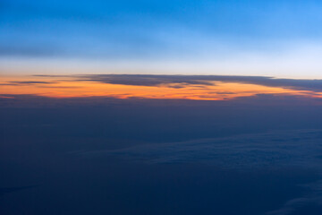 Fototapeta na wymiar Clouds sunset plane. Aerial view of the orange-blue evening light from the airplane window. Panorama cloud landscape stratosphere. The concept of freedom and independence of travel. Sky background