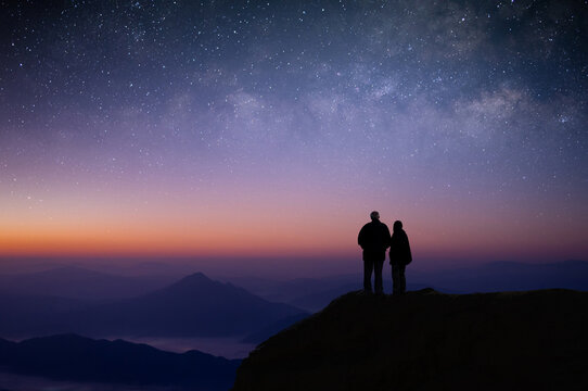 Silhouette of young couple of lovers watched the star, milky way, night sky on top of the mountain. They enjoyed traveling and was successful when he reached the summit.