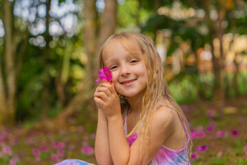 A little girl in a beautiful pink dress in the park, she holds a pink mallow flower in her hands