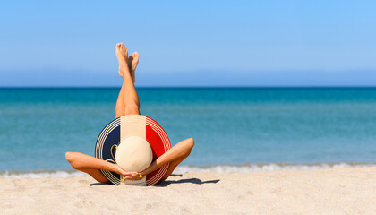 A slender tanned girl on the beach in a straw hat in the colors of the flag of France. The concept of a perfect vacation in a resort in the France. Focus on the hat.