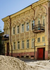 Rostov-on-Don, Russia - September 12, 2019: Facade old two-story building on Donskaya Street. On balcony gypsy woman hangs sheets for drying. On street in front building, piles of sand and dug pits.