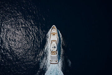 Luxury white mega yacht fast moving on dark water making a trail in the ocean top view. Big white...
