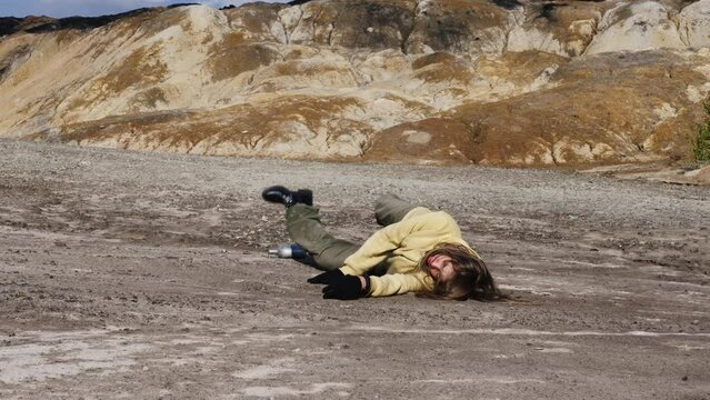 Emaciated girl, wanderer falling in desolate desert place. Tired young woman loses strength in mountains. Exhausted from thirst female tourist is in stone badlands. Post-apocalypse, last human